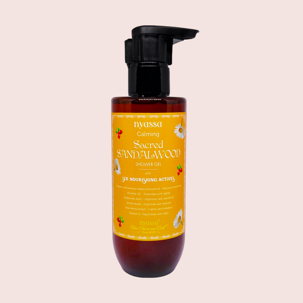 A bottle of Nyassa Sacred Sandalwood Shower Gel with a pump dispenser, featuring yellow and black labeling and white flower graphics.