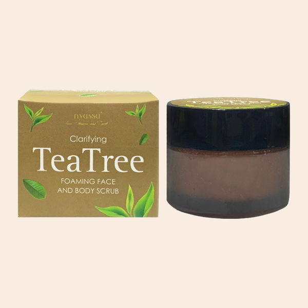 A product image featuring Nyassa Clarifying Tea Tree Foaming Face and Body Scrub with its packaging. The packaging is predominantly brown with the image of tea tree leaves and the product name.