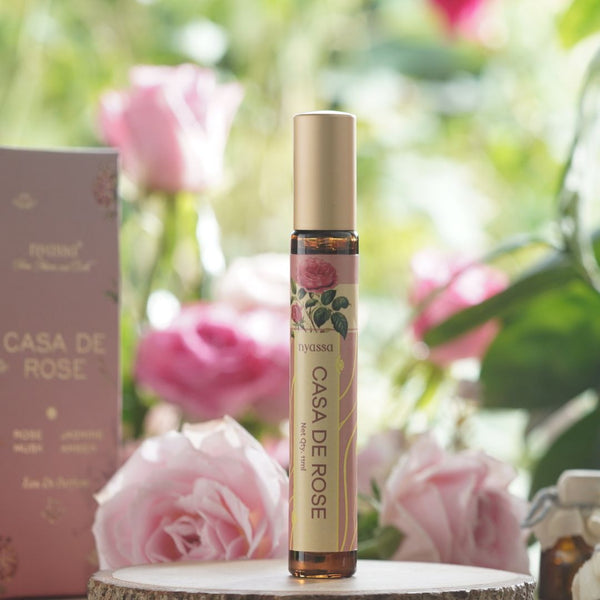 Roll-on bottle of 'Casa de Rose' perfume with pink roses in the background