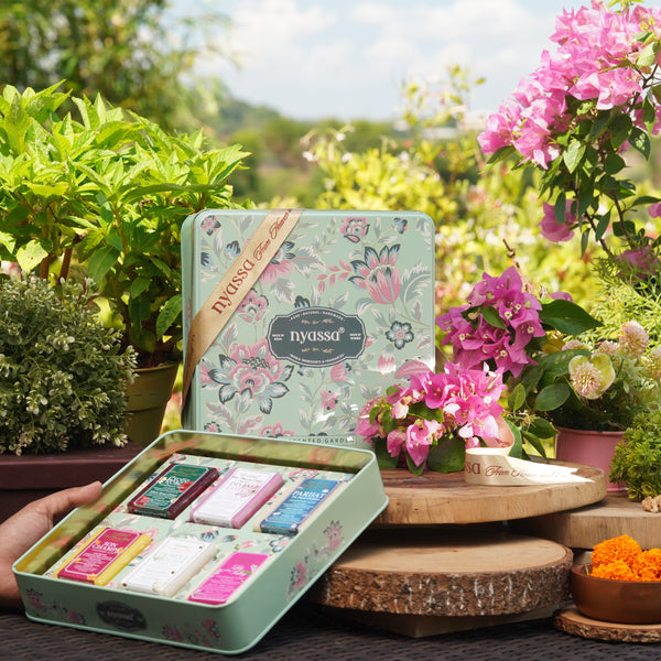Tea set in a tin with floral design held by a hand in a garden setting