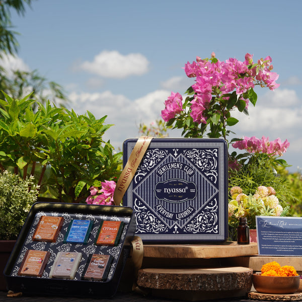 Two makeup palettes with a brand logo on a wooden stand outdoors with flowers and plants.
